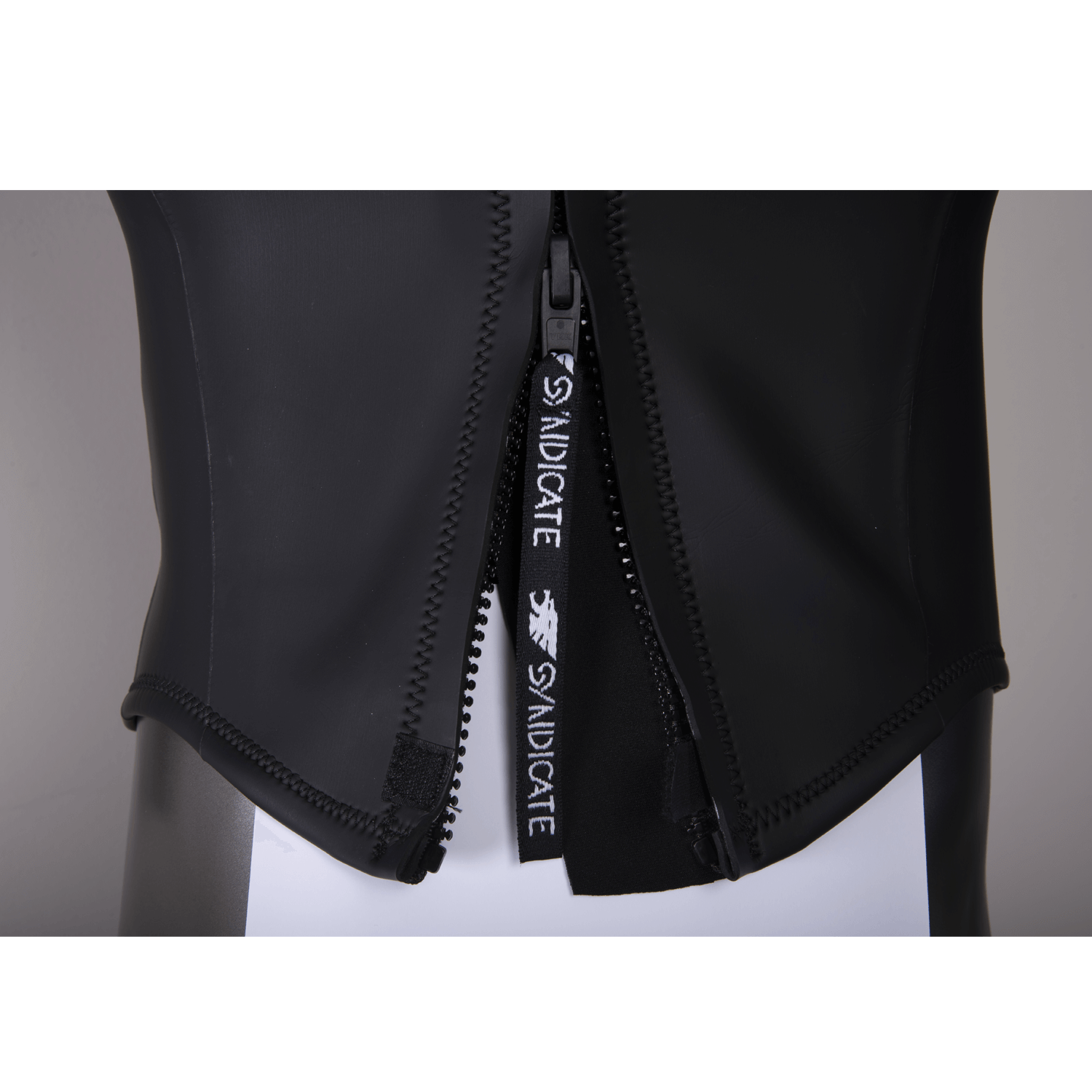 Close-up of the wetsuit zipper, showing the black Syndicate-branded pull tab and reinforced seams.